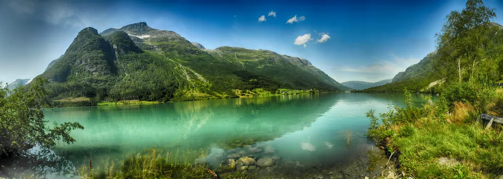 Grüne Berge spiegeln sich in einem türkisfarbenen See.